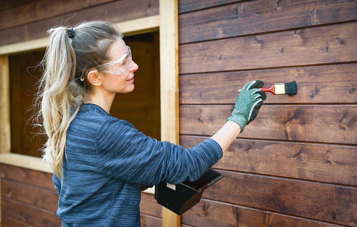 Das Gartenhaus regelmäßig streichen Frau streicht Fassade vom Holzhaus